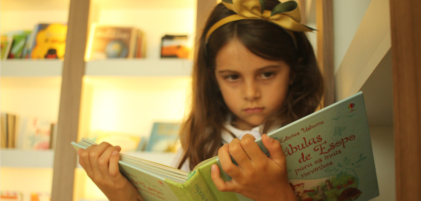 Menina lendo um livro Fábulas de Esopo na escola cristã de educação clássica For Life School